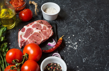 Raw marbled meat steak with ingredients for cooking on dark stone background