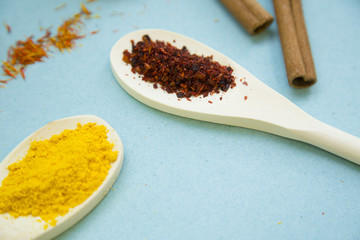 Wooden and plastic spoons with dry spices and fresh herbs on a blue background with copy space, top view, close up
