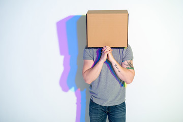 Man with carton on head imploring while looking at camera. Multicolored shadow locating on wall. Entreaty concept. Copy space