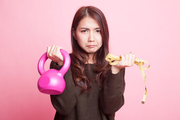 Exhausted  Asian woman with kettlebell and measuring tape.