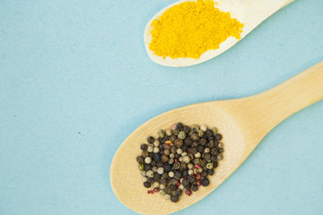 Wooden and plastic spoons with dry spices and fresh herbs on a blue background with copy space, top view, close up