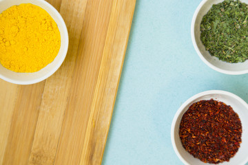 Plastic cups with dry spices and fresh herbs on a wooden cutting board with blue background, top view, close up