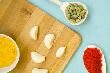 Plastic cup and spoons with dry spices and fresh herbs on a wooden cutting board with blue background, top view, close up