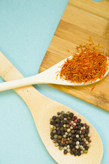 Plastic and wooden spoons with dry spices and fresh herbs on a wooden cutting board with blue background, top view, close up