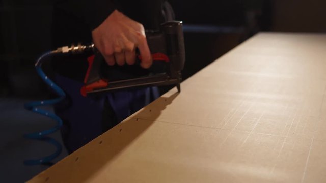 Handy man is using staple gun assembling piece of furniture in a workshop. He is stapling really fast.