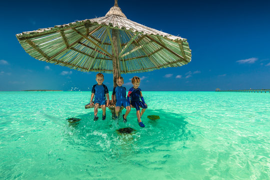Three little boys under beach umbrella in the ocean, tropical Maldives