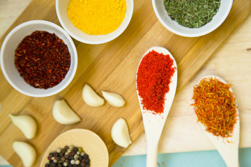 Plastic cups and spoons with dry spices and fresh herbs on a wooden cutting board, top view, close up