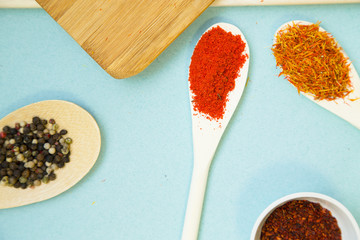 Plastic cups and spoons with dry spices and fresh herbs on a wooden cutting board with blue background, top view, close up