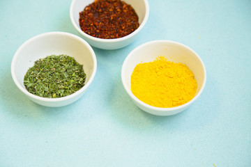 Plastic cups with dry spices and fresh herbs on a blue background with copy space, top view, close up