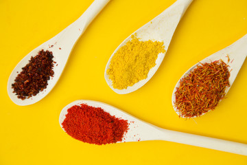 Wooden and plastic spoons with dry spices and fresh herbs on a yellow background with copy space, top view, close up