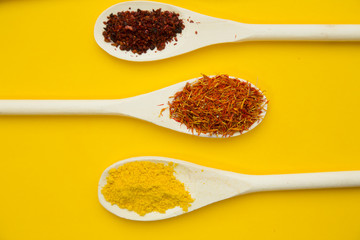 Wooden and plastic spoons with dry spices and fresh herbs on a yellow background with copy space, top view, close up