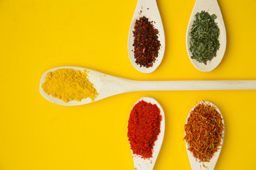 Wooden and plastic spoons with dry spices and fresh herbs on a yellow background with copy space, top view, close up