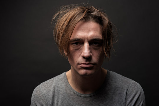 Portrait of exhausted sad guy with shaggy hair standing and looking at camera with apathy. Isolated on background