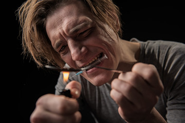 Fototapeta premium Young sad narcomaniac preparing dose of hop. He is holding syringe with teeth. Focus on male expression. Isolated on background