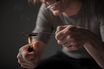 Close up of male arms melting drugs on fire. Isolated on background. Focus on spoon