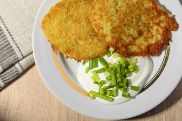 Homemade fried potato pancakes with sour cream and green onions on a plate