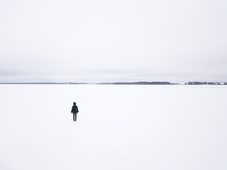 Lonely woman standing on the edge of a snow covered frozen lake. Tartu, Estonia.