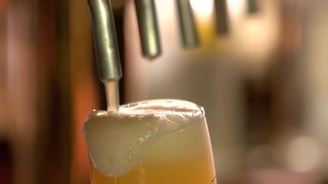Close up light beer overfilling glass, slow-mo. Pouring a pint of draft beer from the crane.