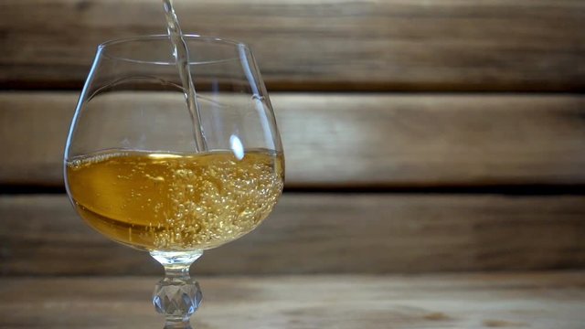 Slow motion pouring a cognac or brandy into glass on wooden background