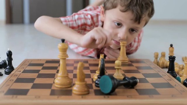 little boy lies on the floor and plays chess