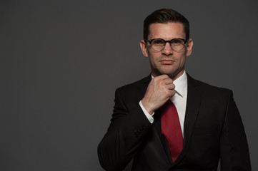 Portrait of successful businessman in formal attire and glasses correcting his necktie looking at the camera on gray background. Place for text