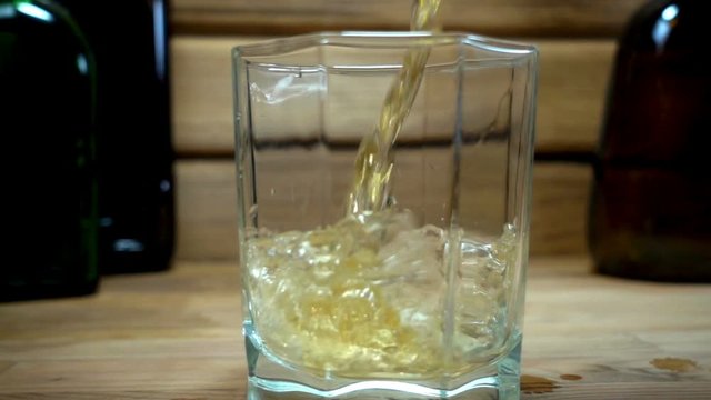 Slow motion, pouring whiskey into the glass on a wooden table with bottles in the background.
