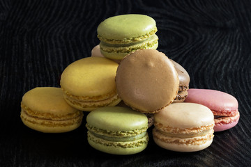 Macarons de couleurs différentes en tas sur fond noir