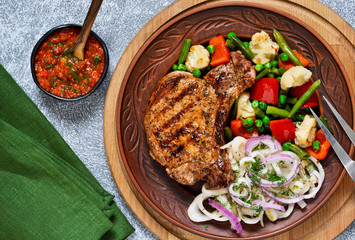 Fried steak with pickled onion and grilled vegetables on a concrete background.