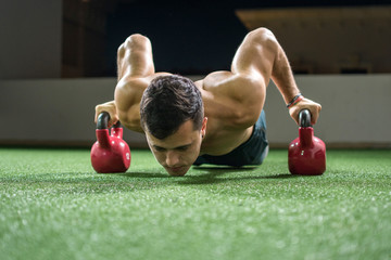 Handsome muscular man doing push ups on kettle bells at the outdoor gym at night.