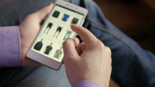 A man looks at the goods in the online clothing store. People using Smartphone, online shopping. The screen is blurred. Close-up. 4K UHD.