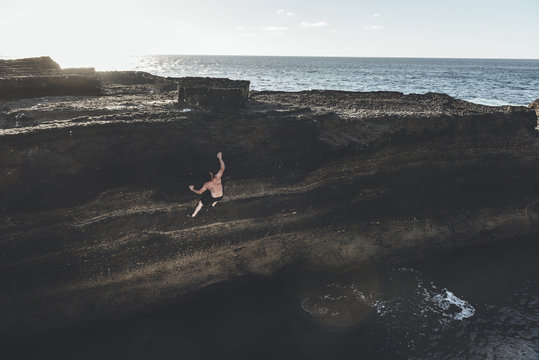 Mature climber climbing without ropes in a seacliff close to the water and lens flare