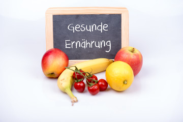 Obst und Gemüse vor einer Tafel auf der gesunde Ernährung steht