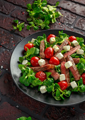 Juicy Beef Sirloin Steak Salad with roasted tomatoes, feta cheese and green vegetables in a black plate. healthy food