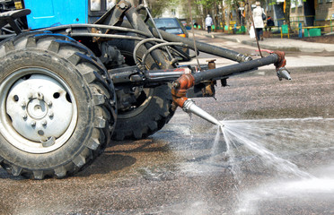 Cleaning sweeper tractor pours water on the asphalt, cleaning the city street.