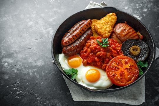 Full English breakfast with bacon, sausage, fried egg, baked beans, hash browns and mushrooms in rustic skillet, pan.