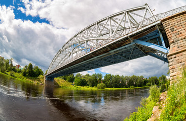 Obraz premium First in Russia steel arch bridge on river Msta in sunny summer day. Was built in 1905. Borovichi, Russia