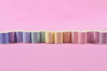 Flat lay of colored thread rolls for sewing on pink background, Sewing and needlework concept.