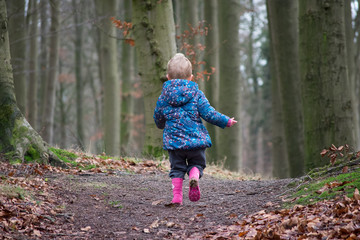 Little girl climbing a small hill. Wearing blue jacket and pink boots.