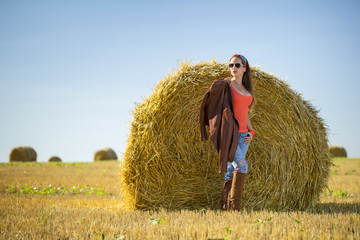 Naklejka na ściany i meble Pretty girl in red t-short and brown jacket stay in front of big roll on the wheat field