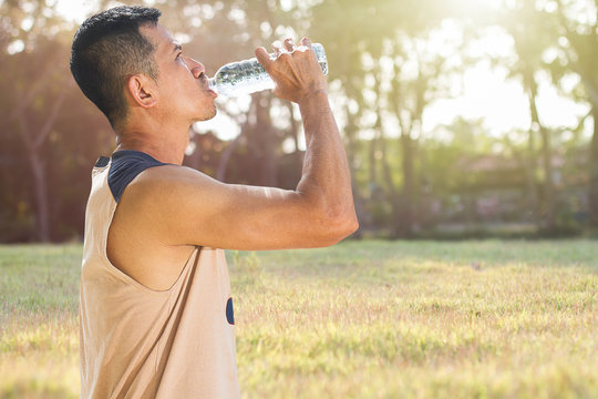 Man drinking water from bottle after running in a park