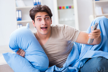 Fototapeta premium Man watching tv from bed holding remote control unit