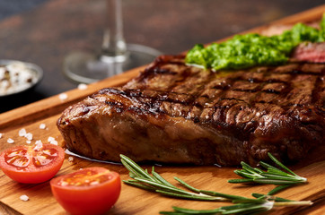 Grilled Black Angus Steak with tomatoes, garlic with chimichurri sauce on meat cutting board.