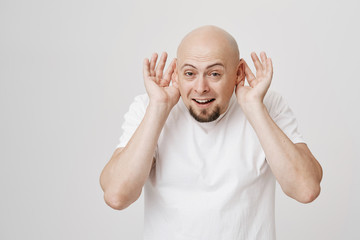 Funny and tricky bald man with beard holding ears with hands as if perking it, or wanting to hear...