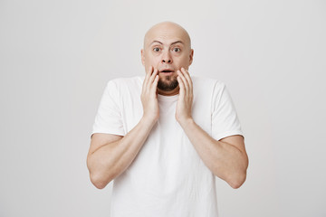 Shocked and surprised bald bearded father holding hands near mouth and look with widened eyes at...
