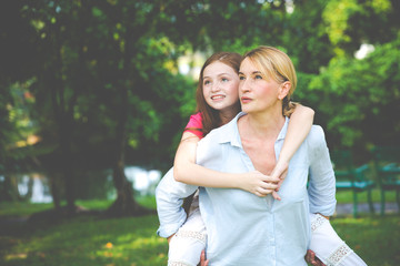 Fototapeta premium Small happy girl enjoying a piggyback ride on her mothers back