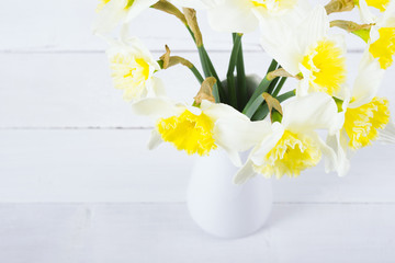 white daffodils at china vase on bright wood table