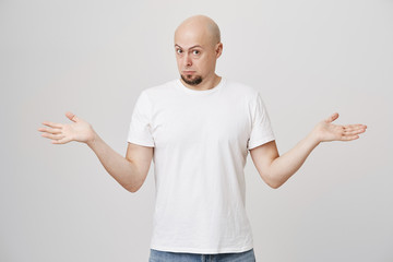 Portrait of handsome bald bearded man spreading hands and bending head towards camera, being...