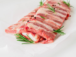 raw pork ribs with seasoning  rosemary, pepper on white parchment paper, side view