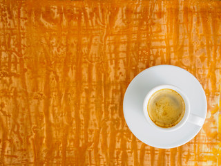 black frothy coffee with foam in white cup with plate on bright copper metal table, top view, empty space for text