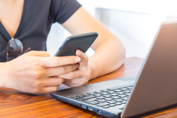 Fototapeta premium Woman playing a smart phone with laptop placed in front.